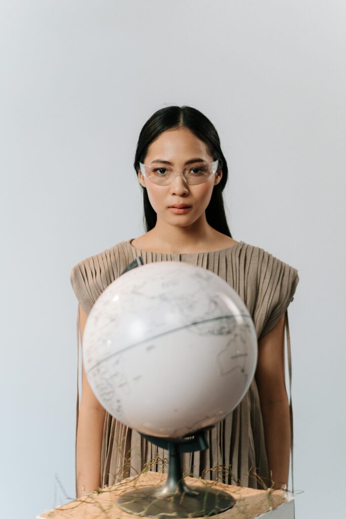 Portrait of an Asian woman wearing safety glasses, examining a globe on a white background.