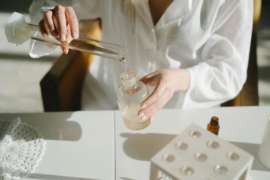 A scientist in white lab coat pours liquid between glass containers on a laboratory table.