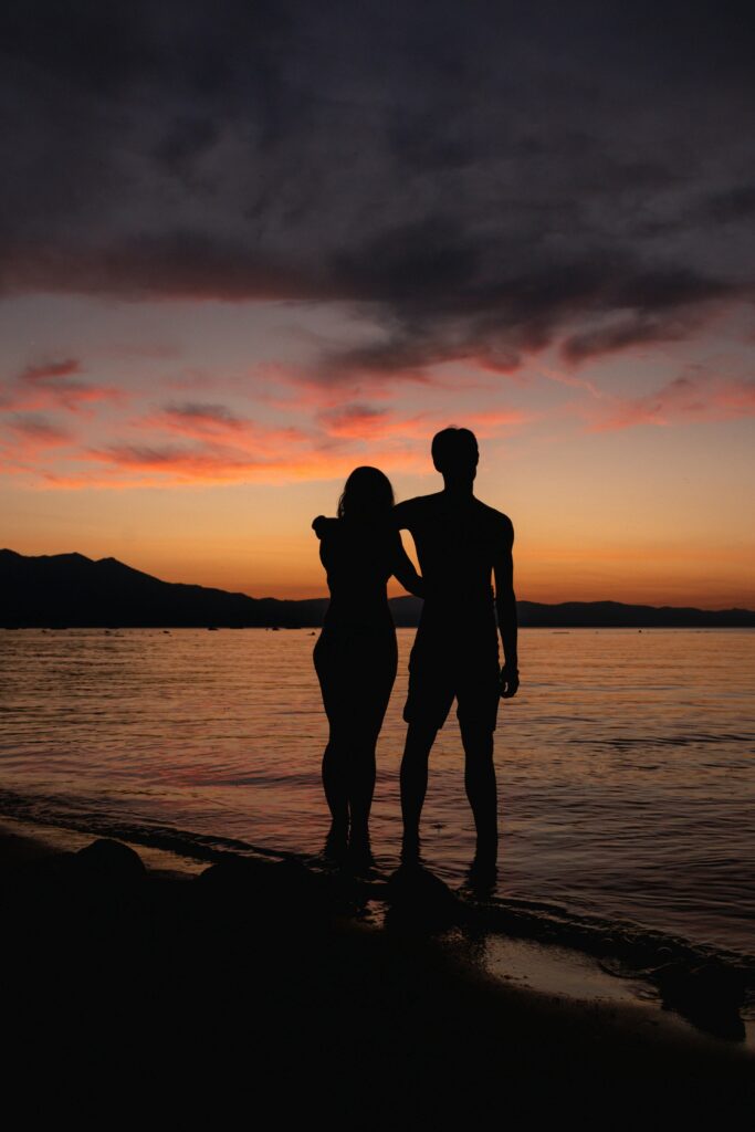Silhouette of a couple embracing by the ocean at sunset, showcasing a dramatic sky.
