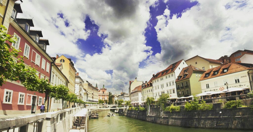 Scenic view of colorful riverside buildings in Ljubljana, showcasing vibrant architecture under dramatic skies.