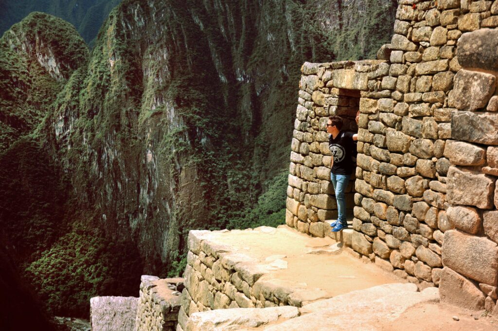 Man at Machu Picchu doorway overlooking lush mountains, capturing Inca architectural marvels.