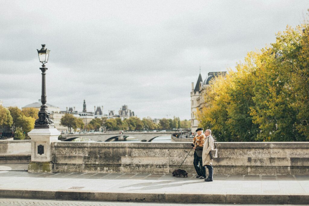 Charming scene of an elderly couple walking their dog on a Parisian bridge during daylight.