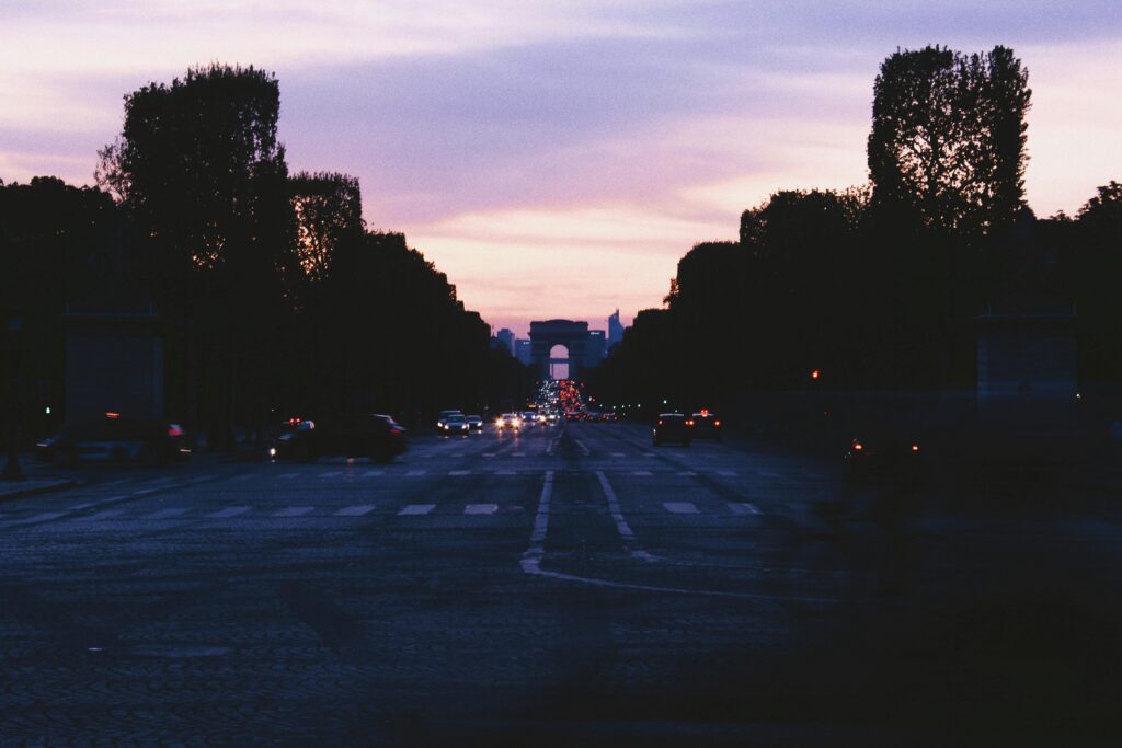 View of a city street at dusk with the Arc de Triomphe in the distance, capturing the city's silhouette.