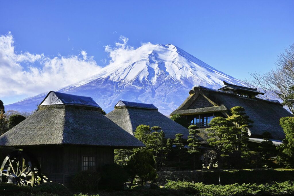 Scenic view of traditional thatched roof houses with Mount Fuji in the background on a clear day.