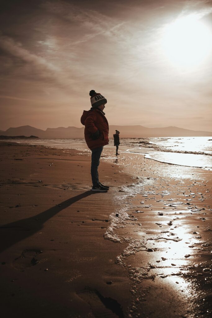 Children enjoy a peaceful sunset on a beach with mountains in the distance.
