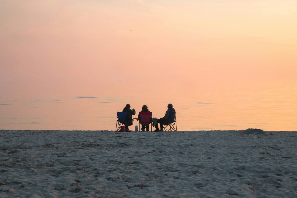 Three people seated on a beach enjoying a serene sunset view.