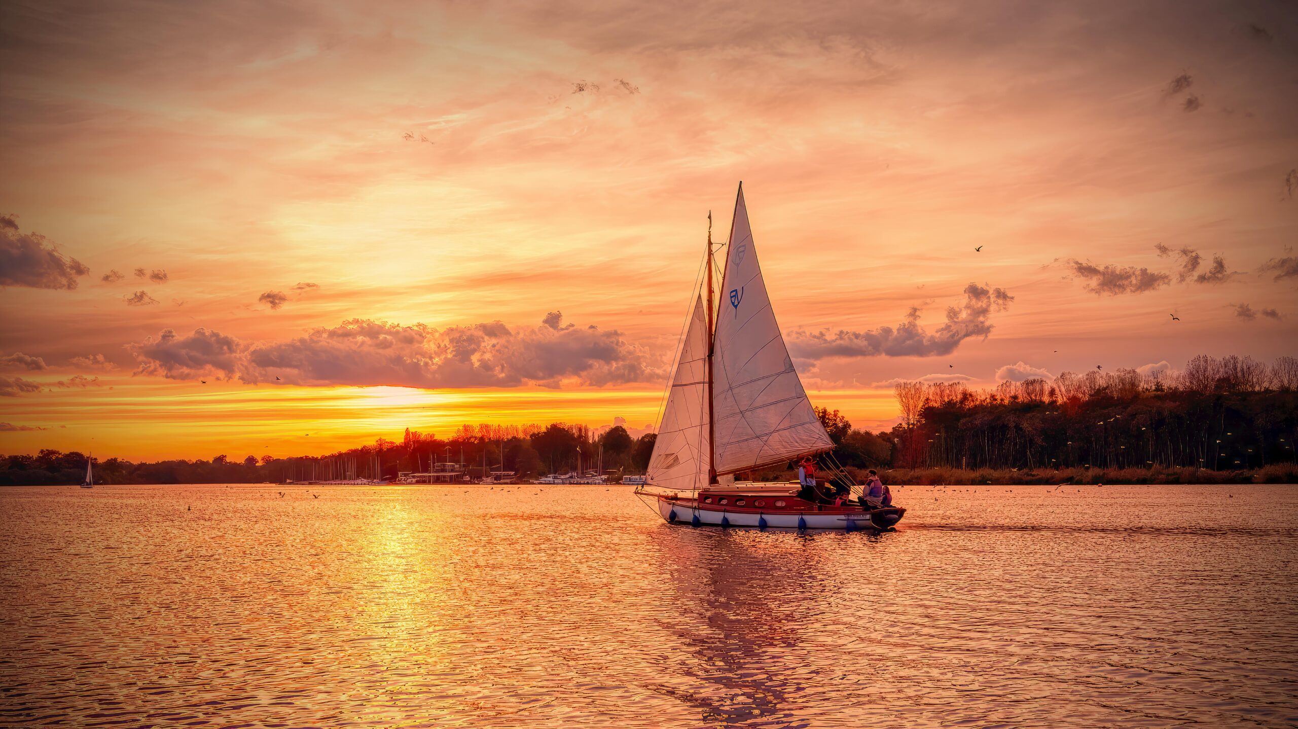 A serene sailboat glides across calm waters at sunset on the Norfolk Broads, England.