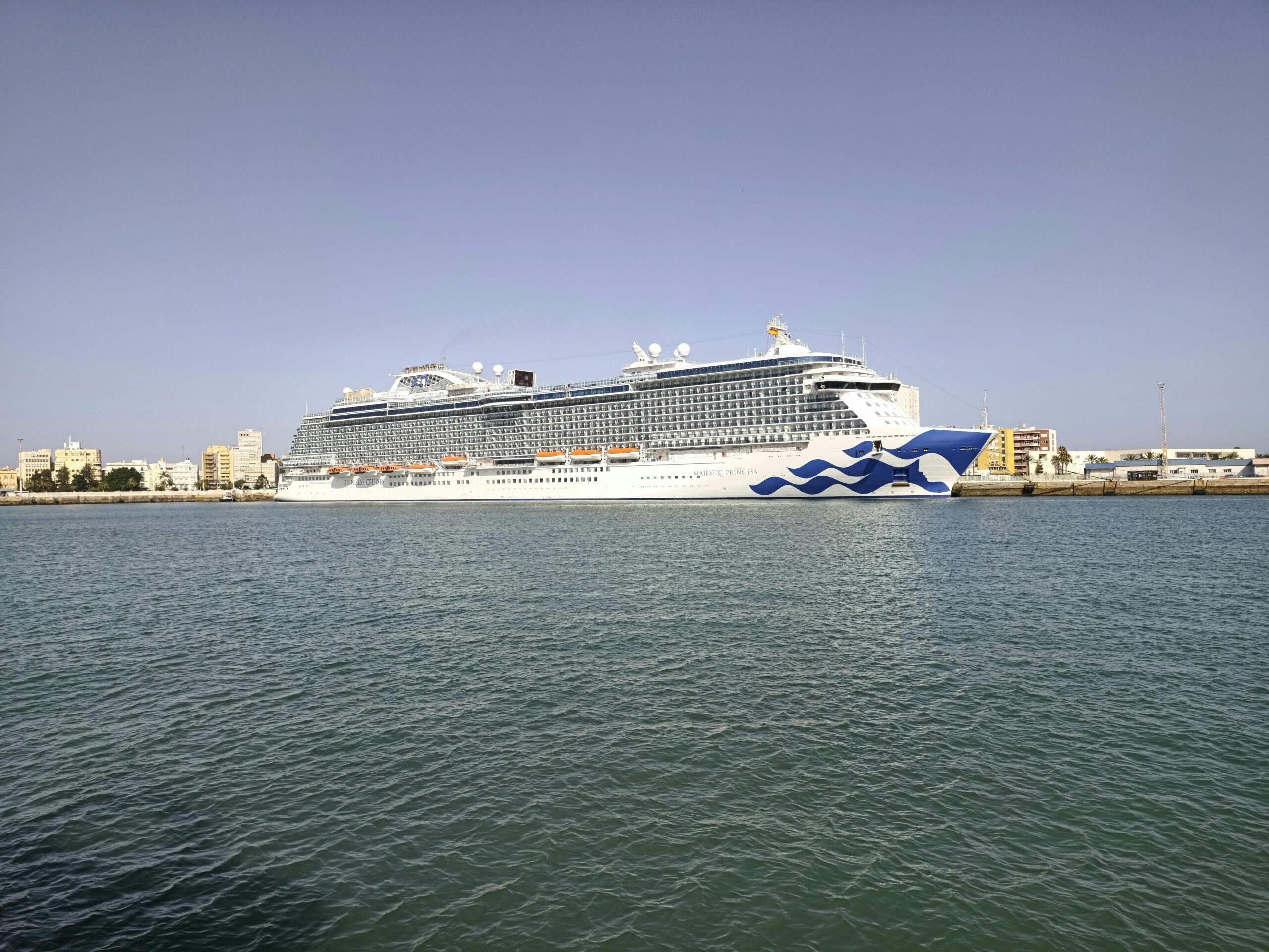 Large cruise ship docked in the scenic harbor of Cádiz, Spain under a clear blue sky.
