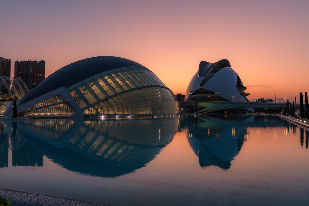 Stunning sunset view of Valencia's iconic City of Arts and Sciences reflecting in calm water.