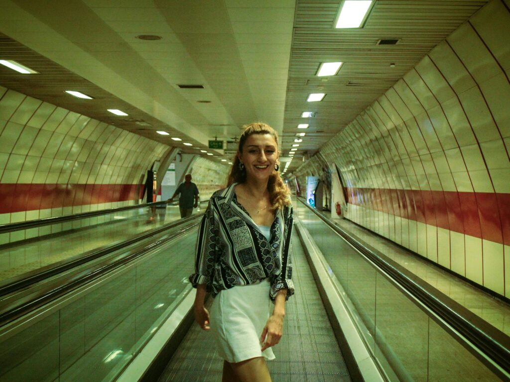 A cheerful woman in fashionable attire walks on an airport moving walkway.