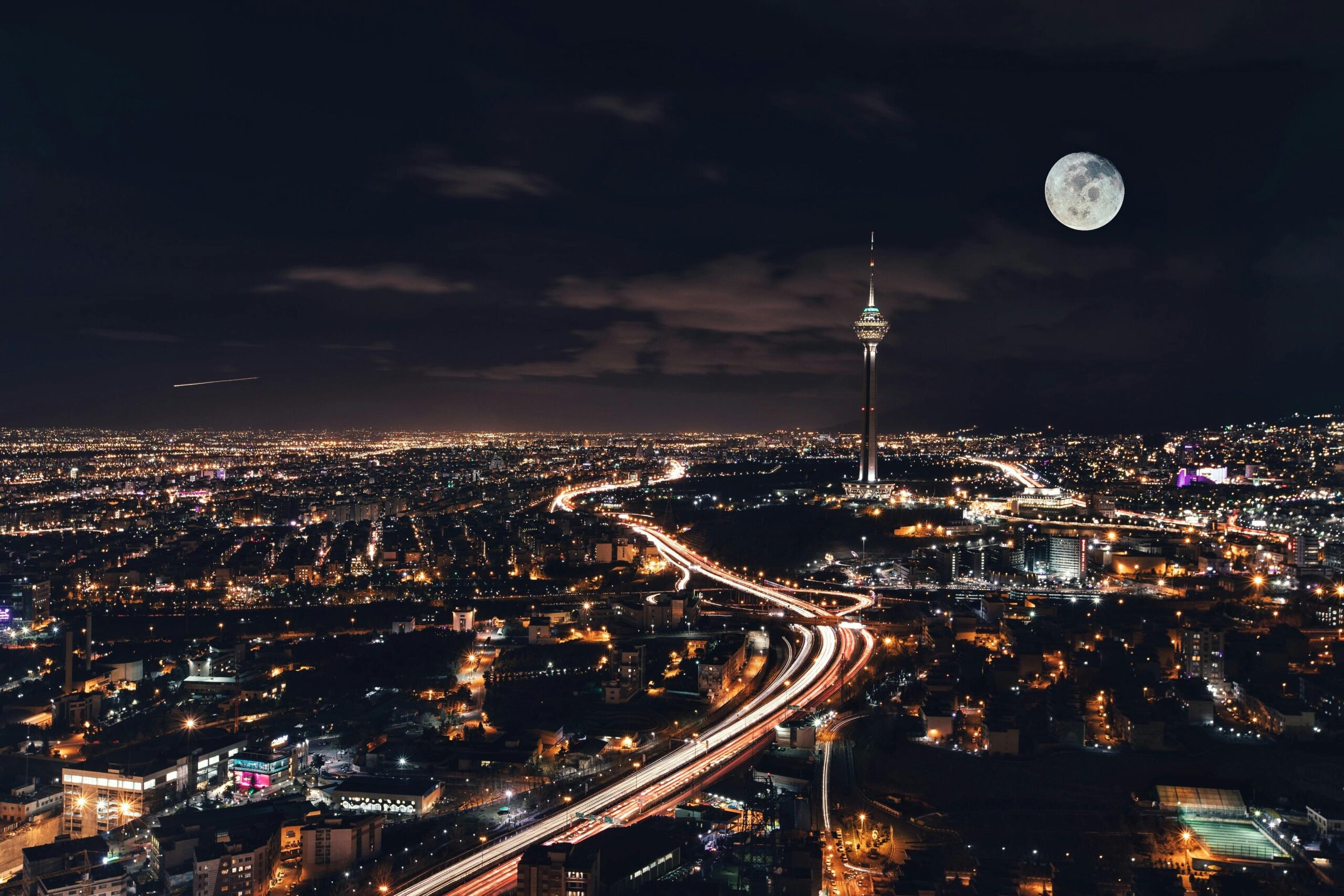 Captivating night view of Tehran's skyline featuring Milad Tower and a full moon.