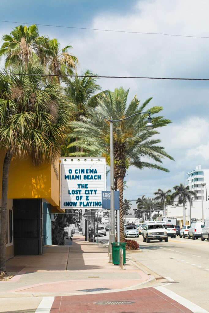 A vibrant street view of O Cinema in Miami Beach with palm trees and a clear sky.