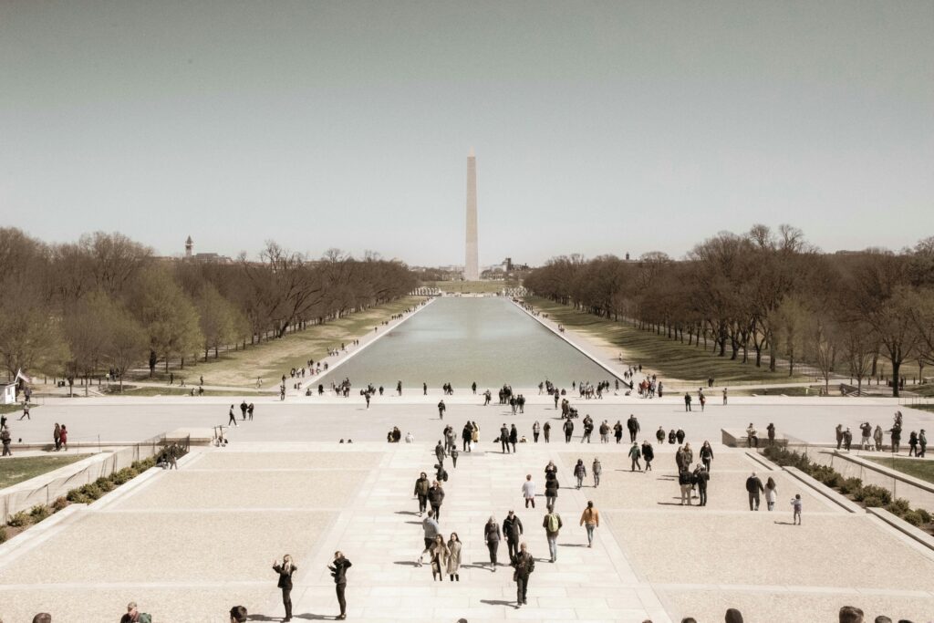 A crowd enjoys a sunny day at the Washington Monument Reflection Pool, a popular tourist spot in Washington, D.C.