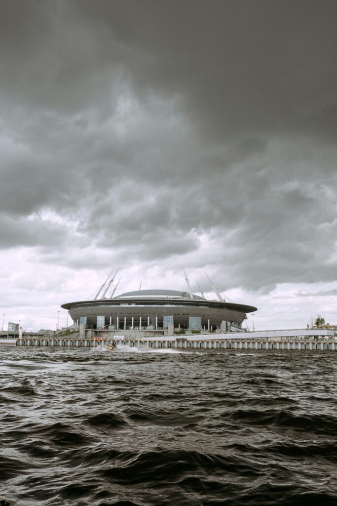A dramatic cloudy sky looms over a modern football stadium along a coastal line.
