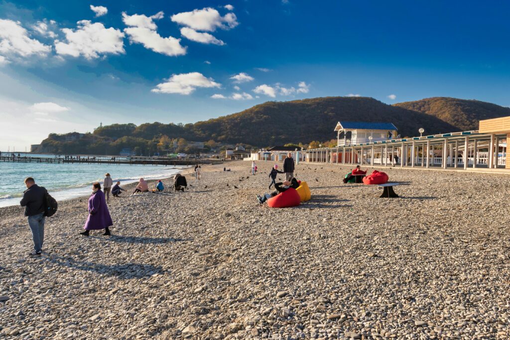 People relaxing on a pebble beach with scenic hills in the background on a clear day.