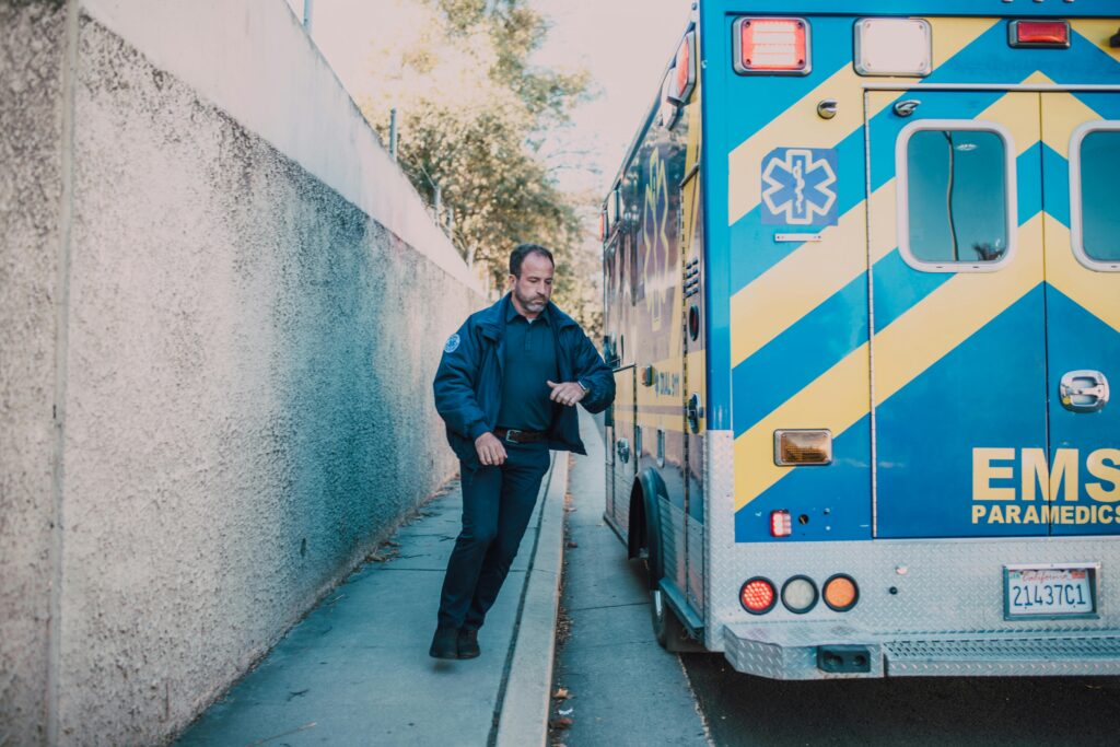 Emergency medical technician beside parked ambulance on roadside in daylight.