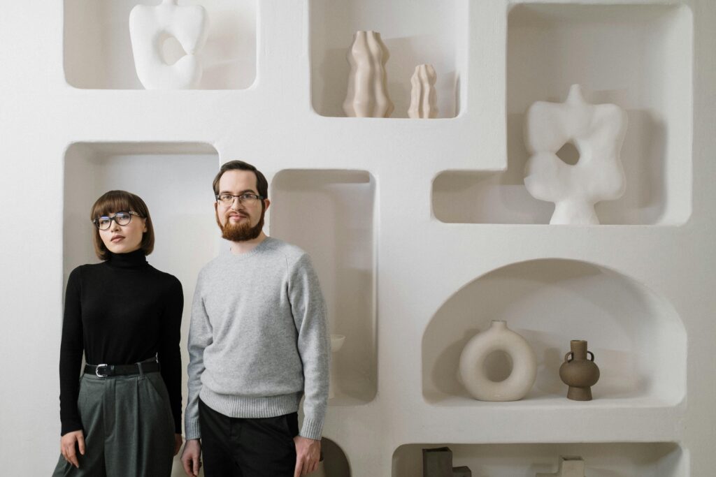 A man and woman stand against a modern art-decorated wall, showcasing minimalist style.