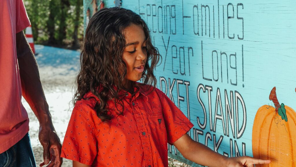 A child in a red shirt interacting with a vibrant outdoor wall mural in daylight.