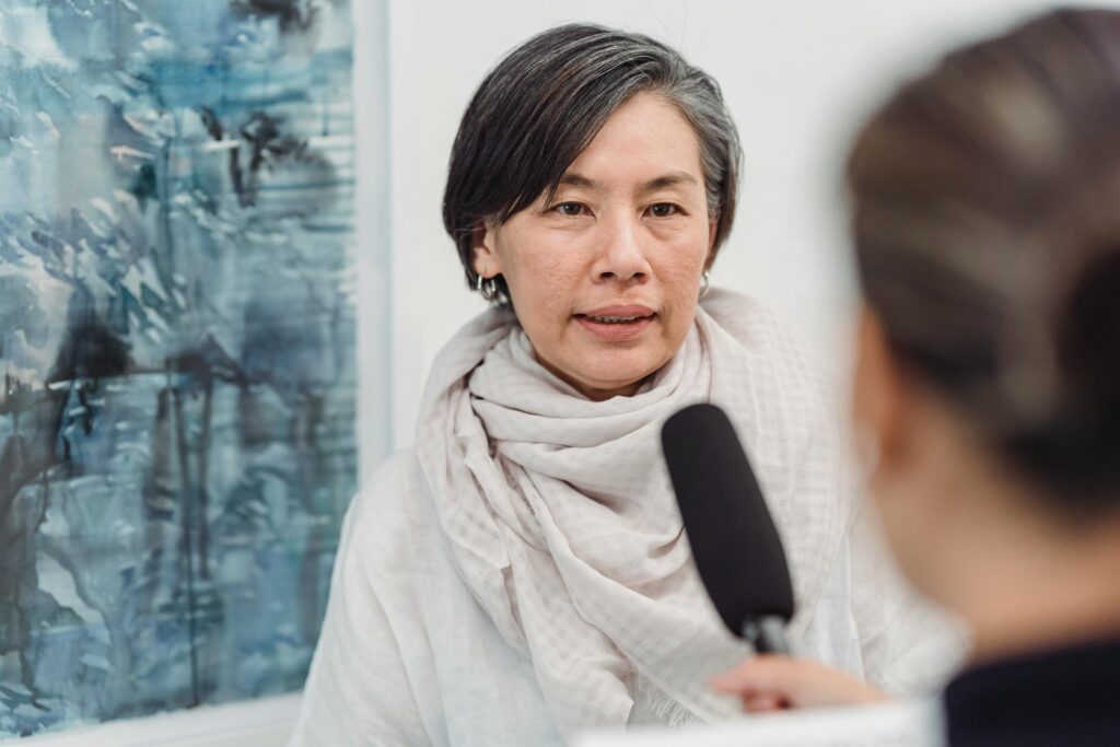 Asian woman in discussion with a journalist at an indoor art gallery.