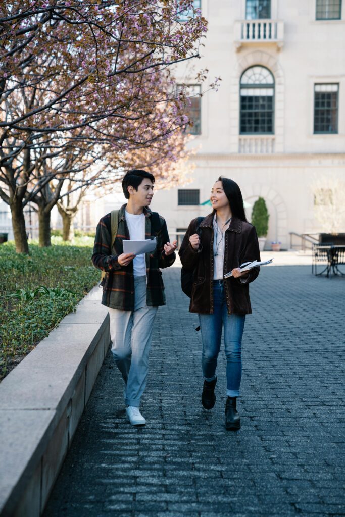 Two students walking on a university campus with papers in springtime.