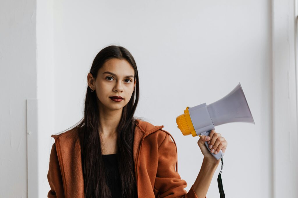 Portrait of a young woman holding a megaphone in a casual setting, conveying empowerment and voice.