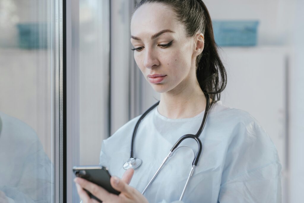 Portrait of a female doctor in a disposable gown using a smartphone in a hospital environment.