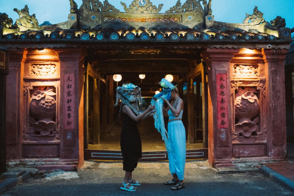 Two people in traditional attire exchanging costumes at an ancient temple during twilight.