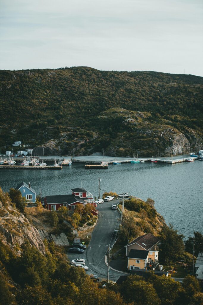 A serene coastal village with boats docked by the bay and lush green hillside backdrop.
