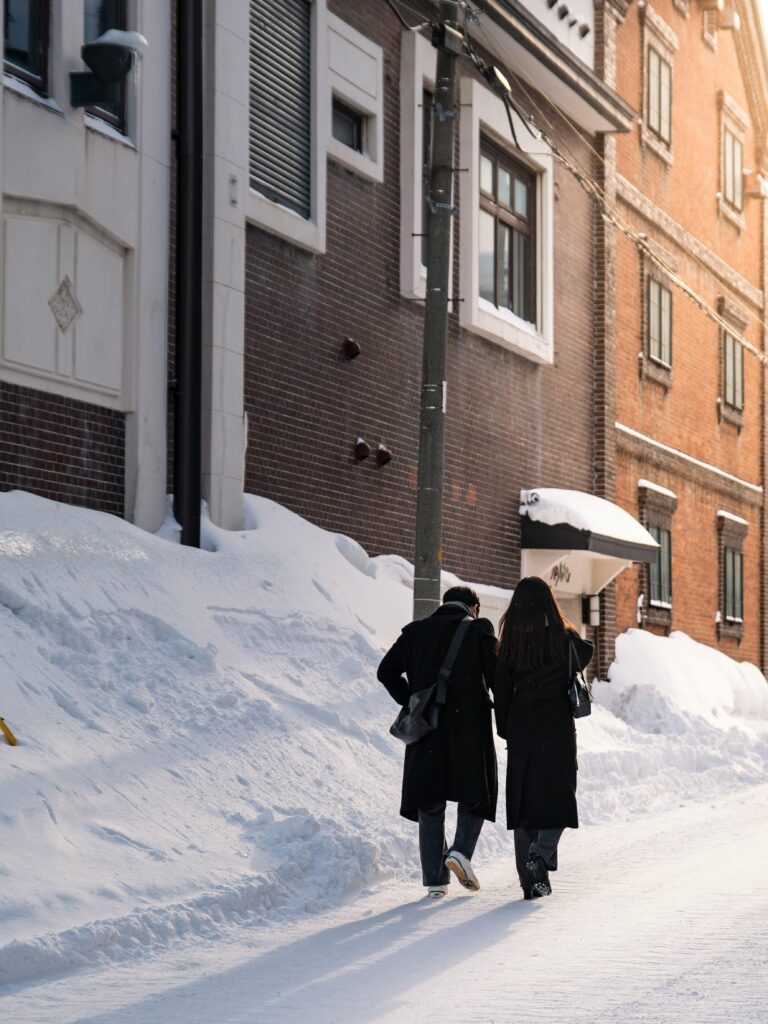 A couple walks down a snowy street in Otaru, Japan, surrounded by winter architecture.