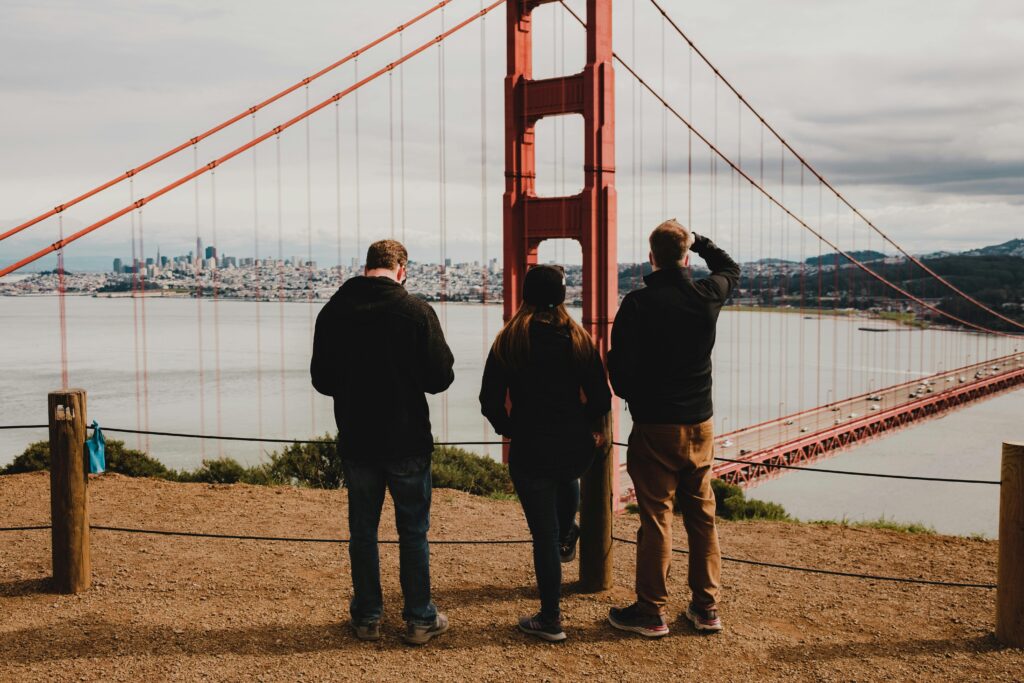 Three individuals admire the Golden Gate Bridge from a scenic viewpoint on a cloudy day.