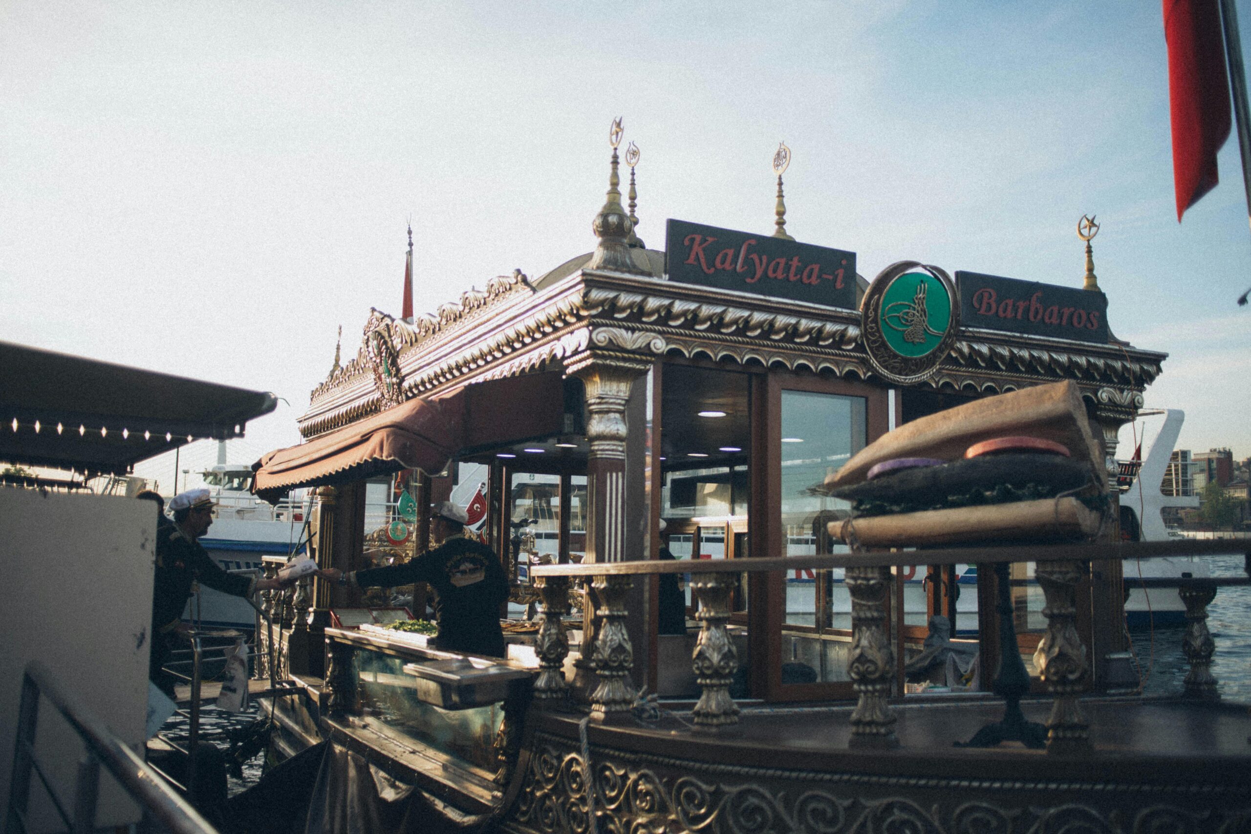 A traditional Turkish boat offering street food, anchored in a city harbor at sunset.