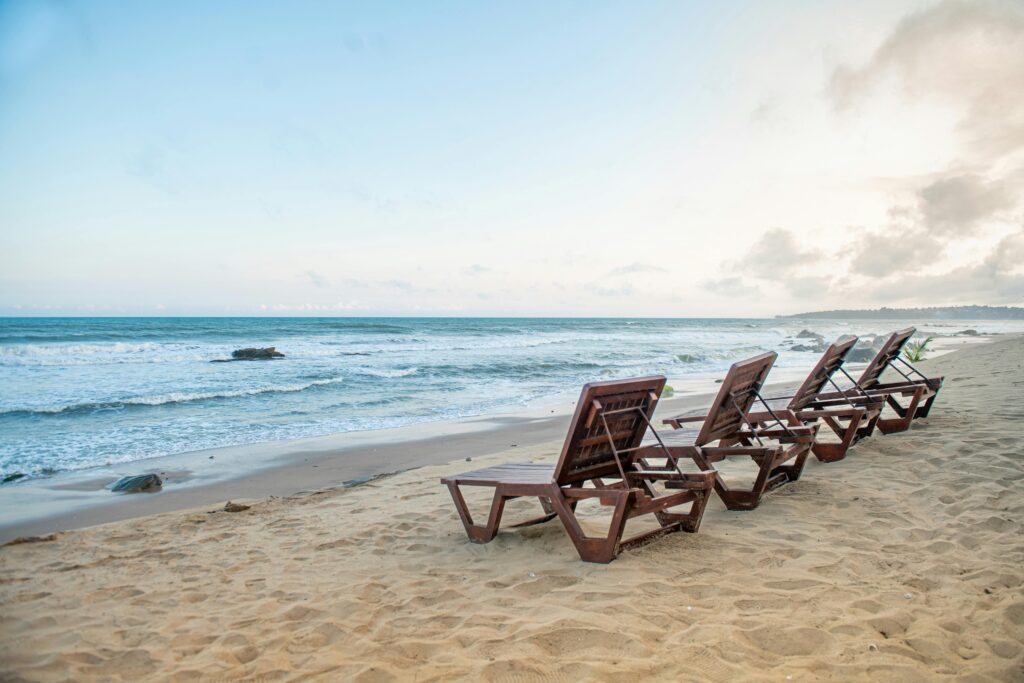 Peaceful beach in Accra, Ghana, featuring wooden loungers on sandy shore against a serene ocean backdrop.