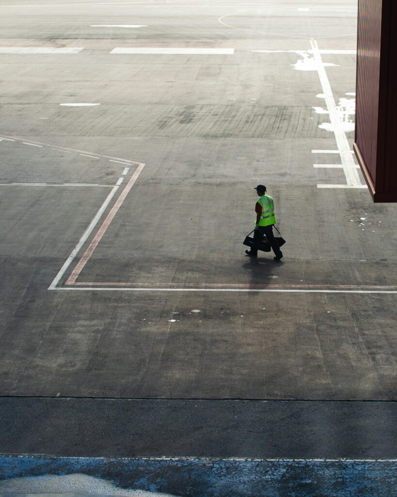 Airport worker in high-visibility gear walking on a sunny airport tarmac in Brazil.