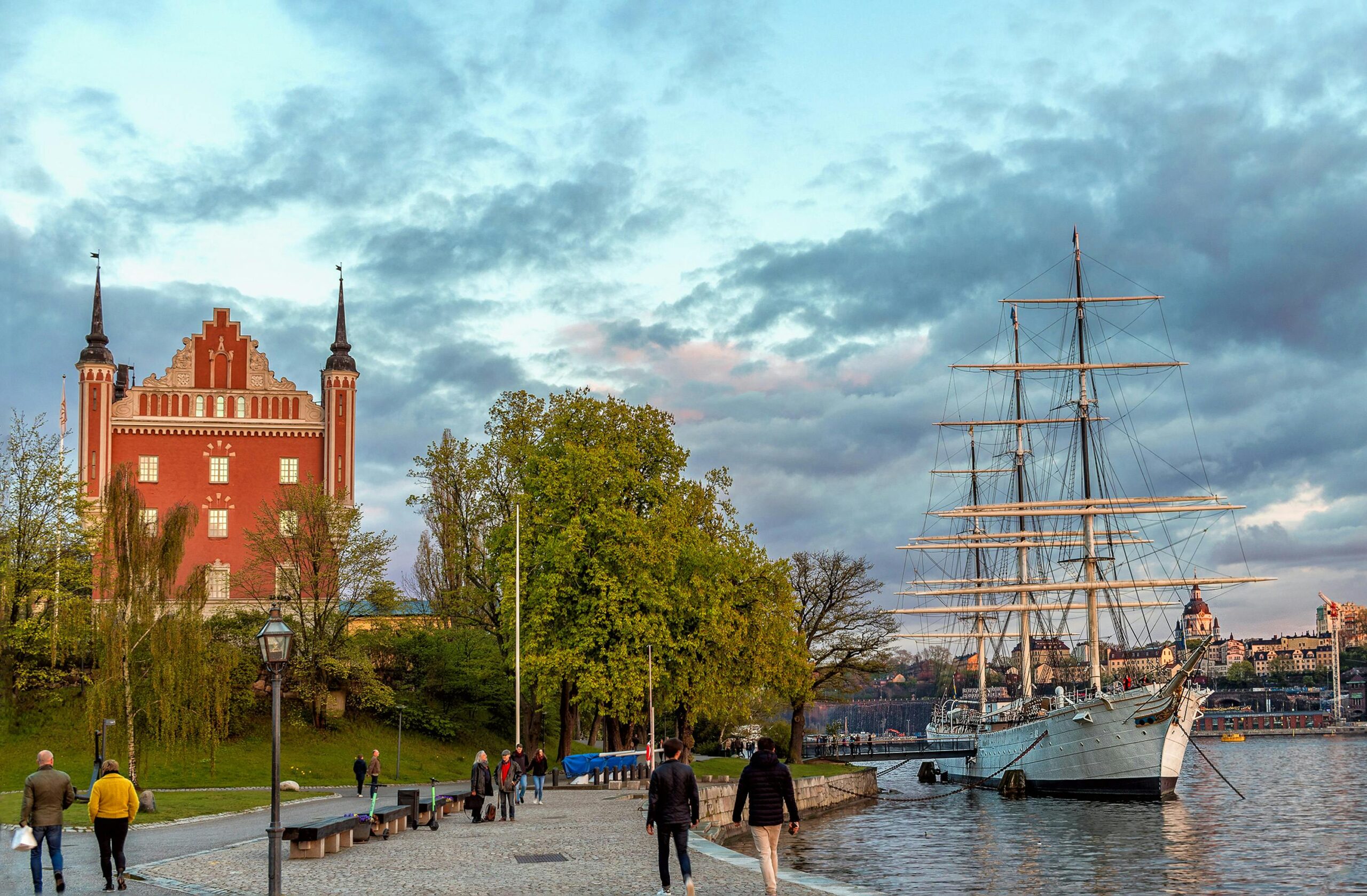 A beautiful waterfront scene in Stockholm with a historic ship and the iconic red building under a cloudy dusk sky.