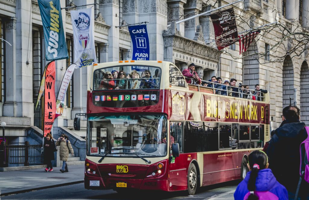 Double-decker bus with tourists sightseeing in downtown New York City on a sunny day.