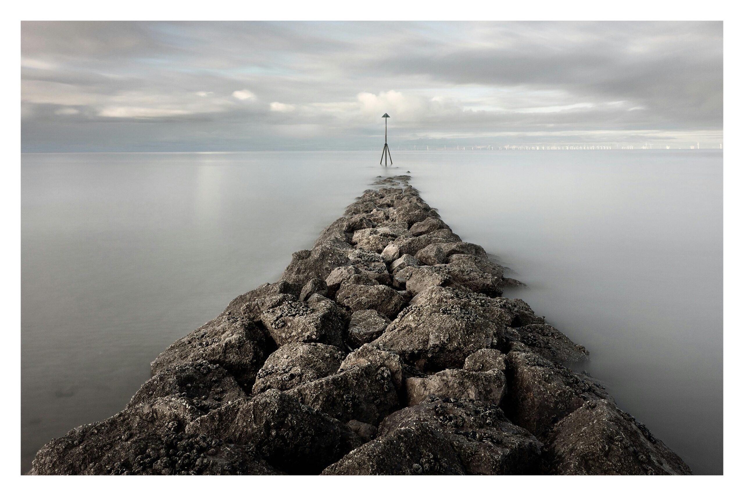A peaceful view of the sea breaker at Rhos on Sea, Wales, with calm waters and a cloudy sky.