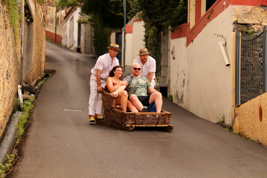 Tourists enjoying a classic toboggan ride down the steep streets of Funchal, Madeira.