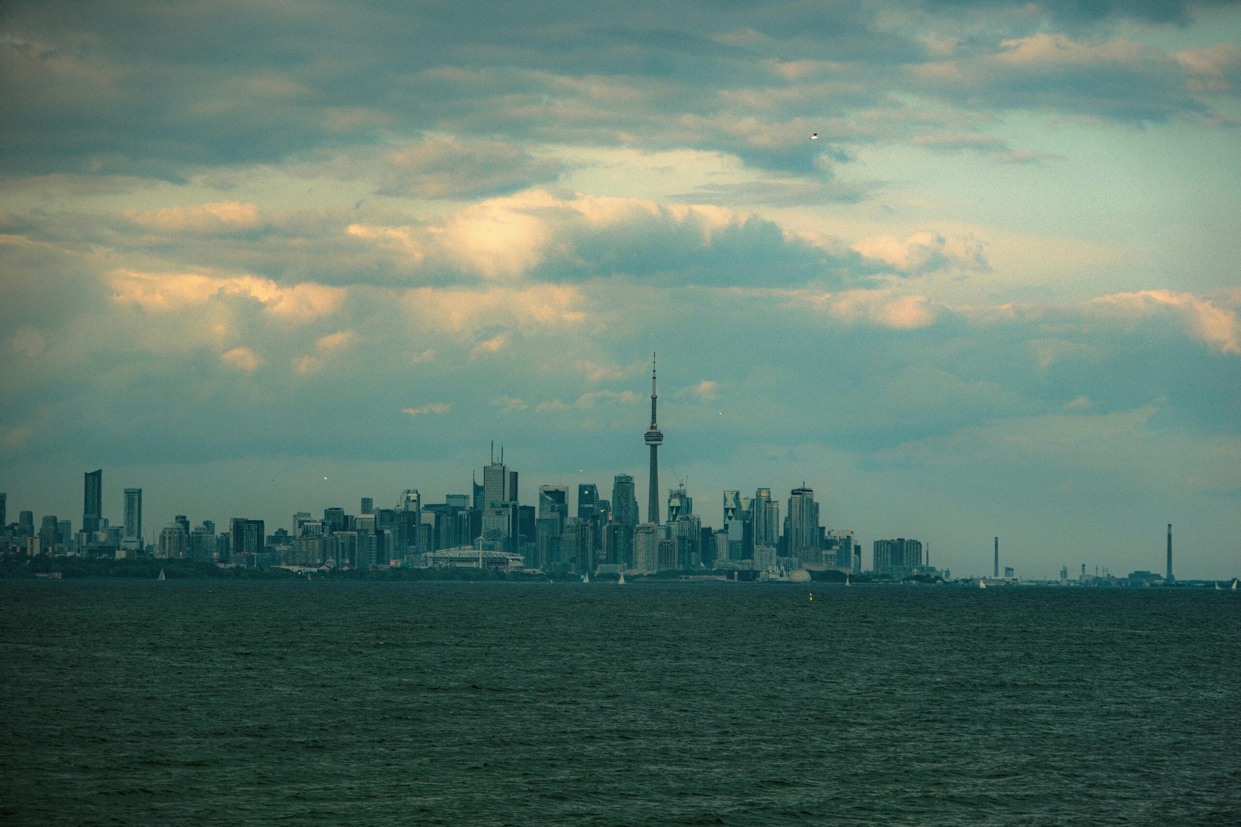 Distant view of Toronto skyline highlighting CN Tower and skyscrapers under a dramatic cloudy sky.