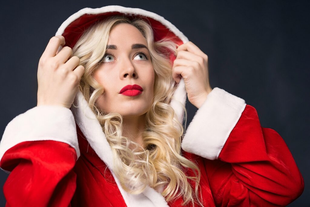 A fashionable woman in a Santa outfit, looking upward with red lips and blonde curls.