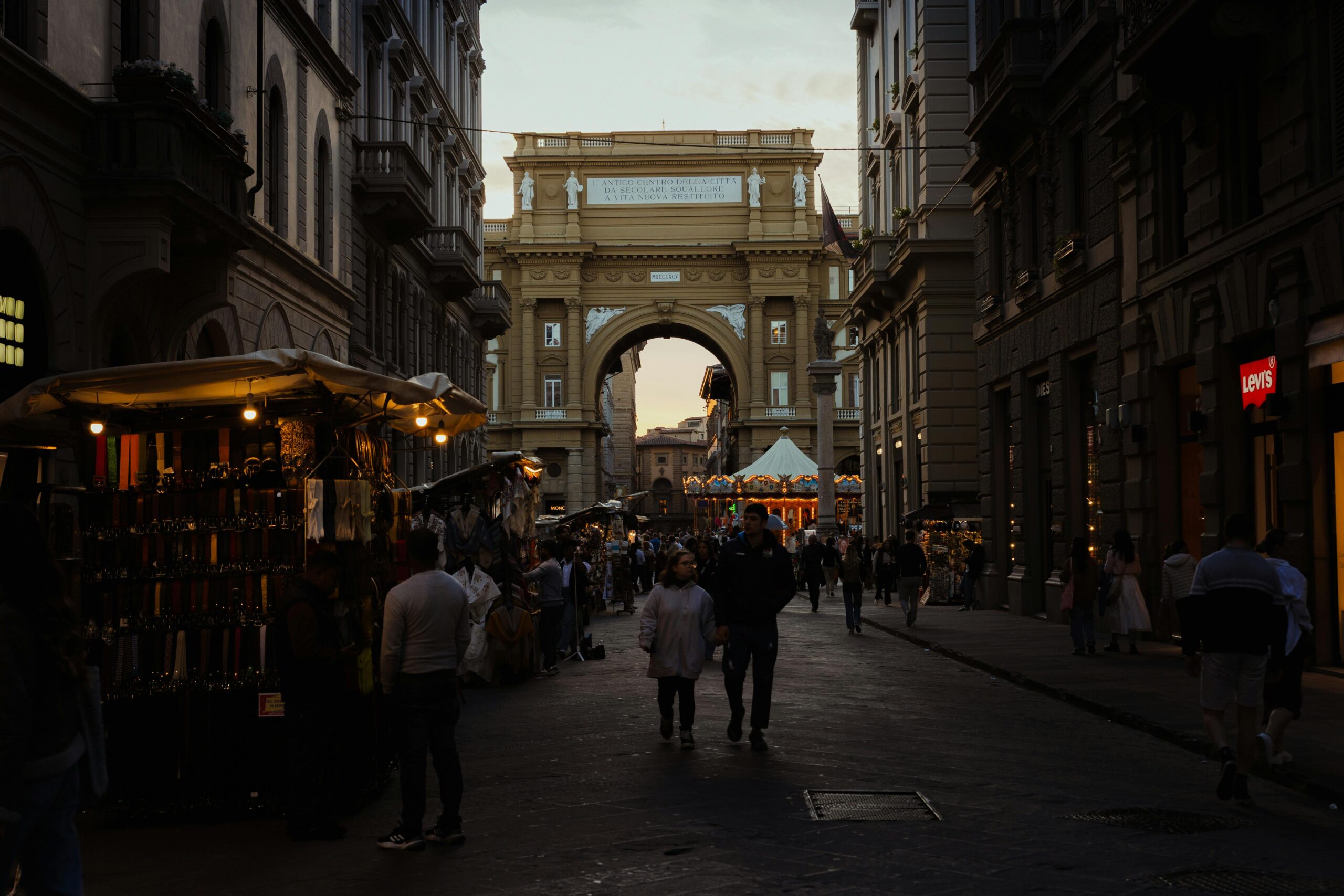 Bustling evening market at Piazza della Repubblica, Firenze with shoppers under the glowing lights.