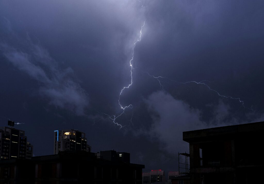 Powerful lightning bolt illuminates a dark cityscape during a nighttime storm.
