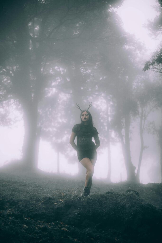Mysterious woman with antlers in a foggy forest setting.