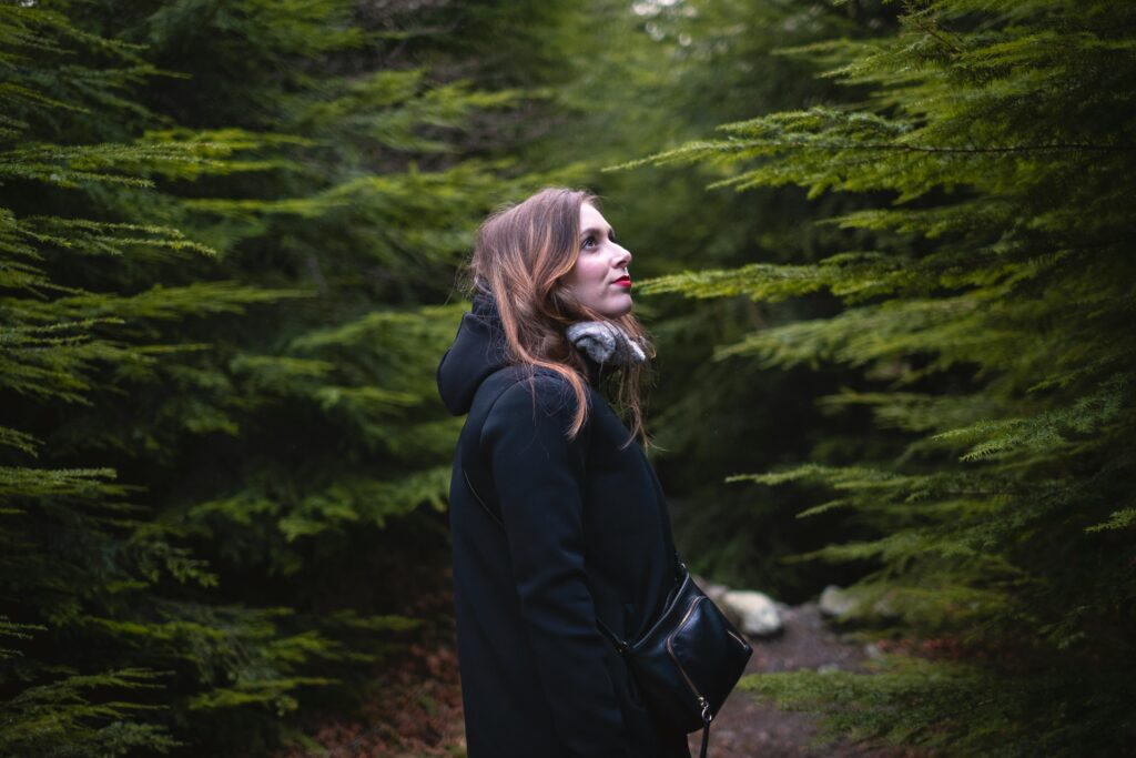 A woman in a black coat explores the lush greenery of Tollymore Forest Park in Northern Ireland.
