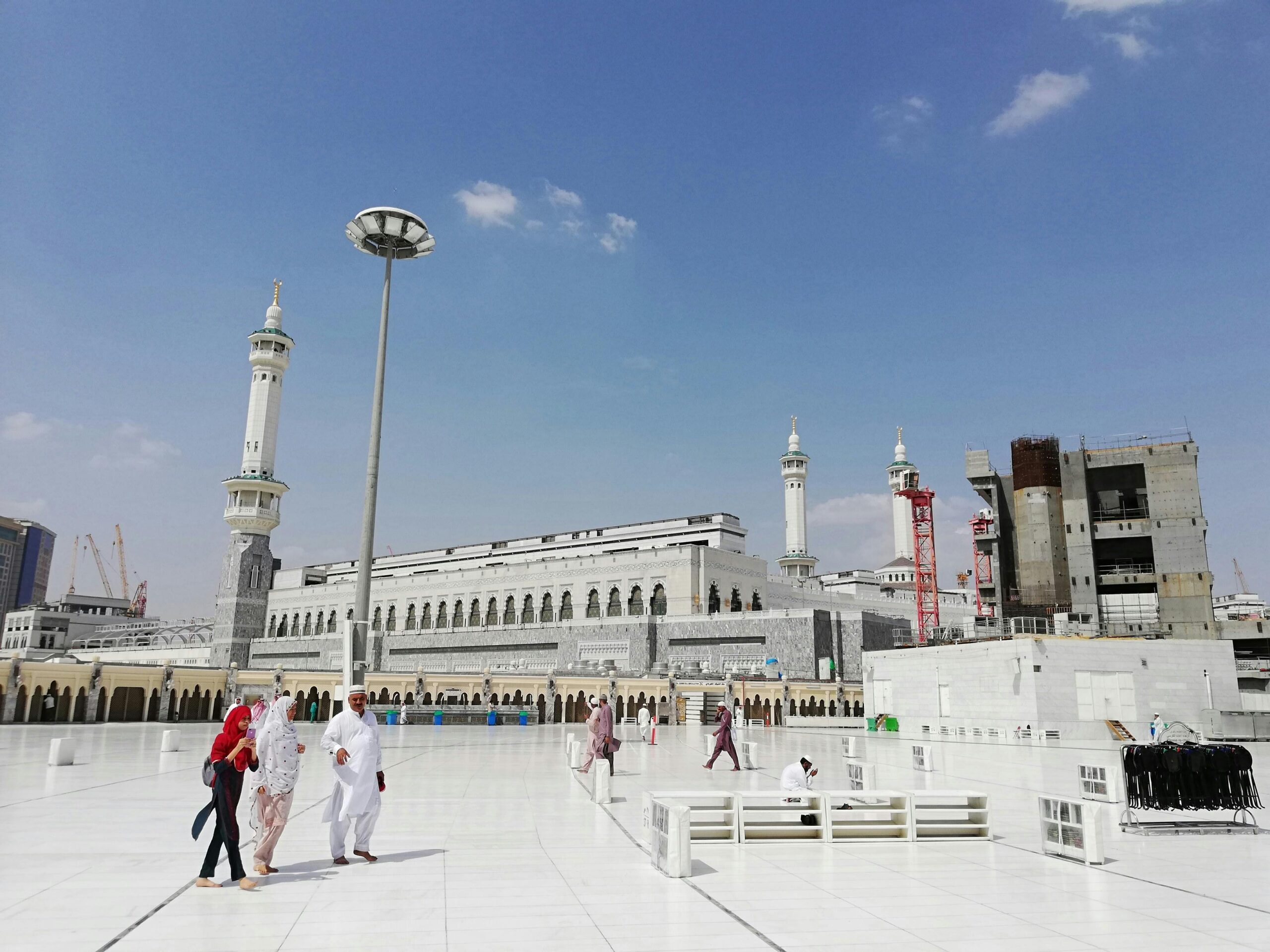 Pilgrims walk in the courtyard of Masjid al-Haram, Mecca, under a clear blue sky.