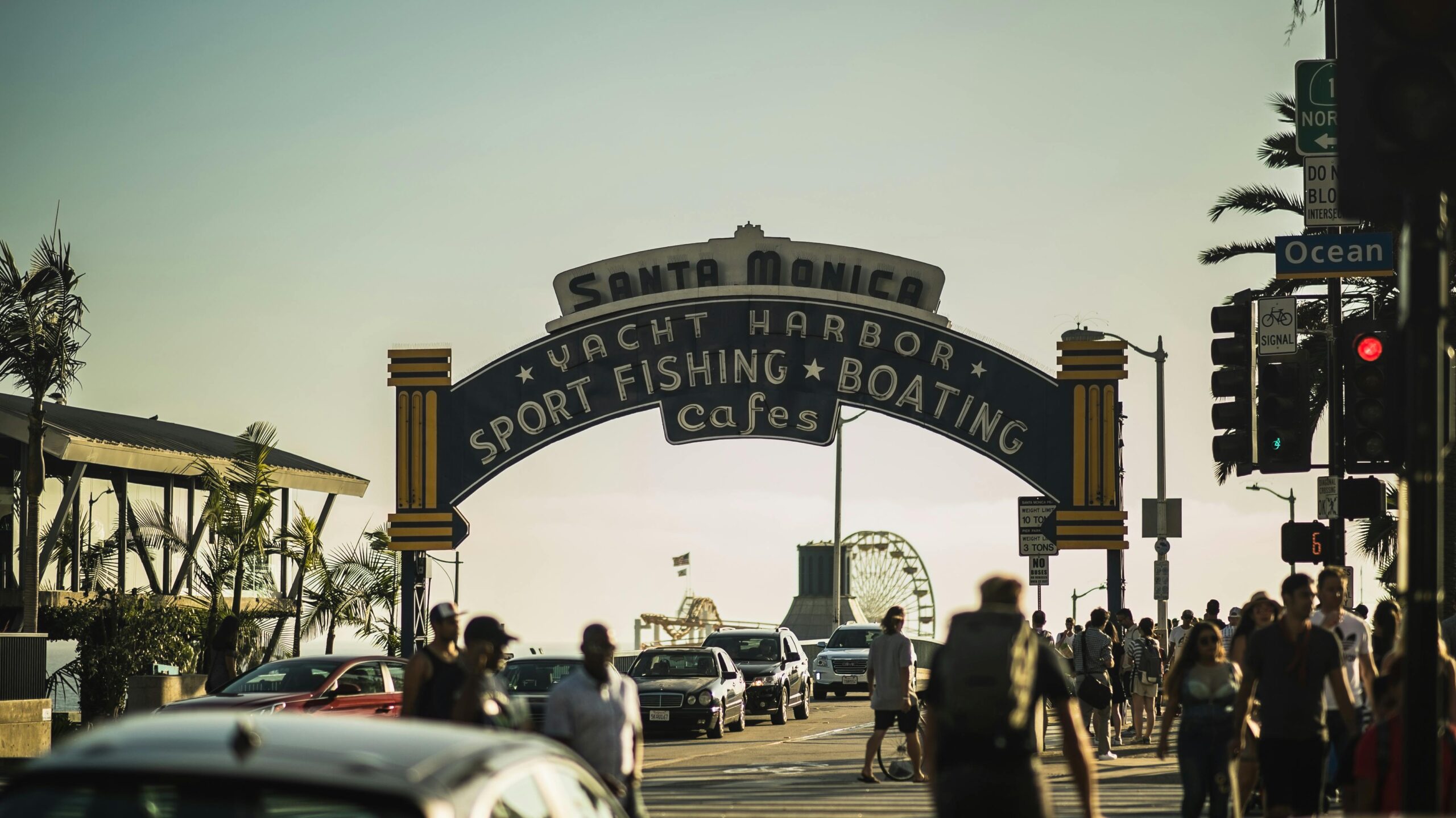 A bustling street scene at the iconic Santa Monica Pier entrance during sunset.