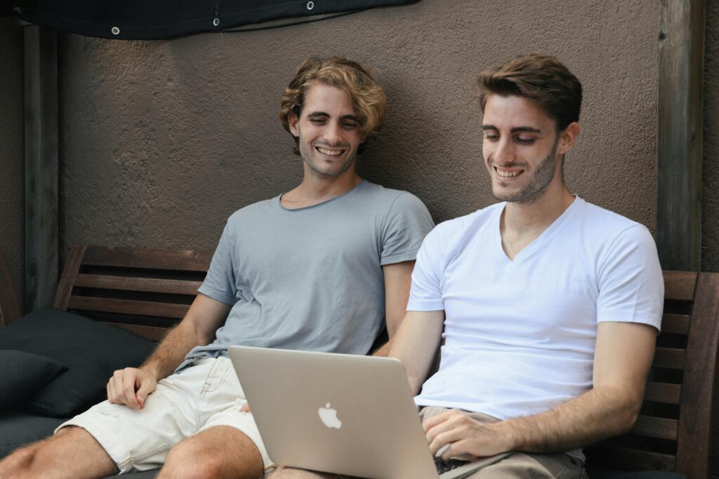 Two friends happily working together on a laptop while sitting on a bench outdoors in Barcelona.