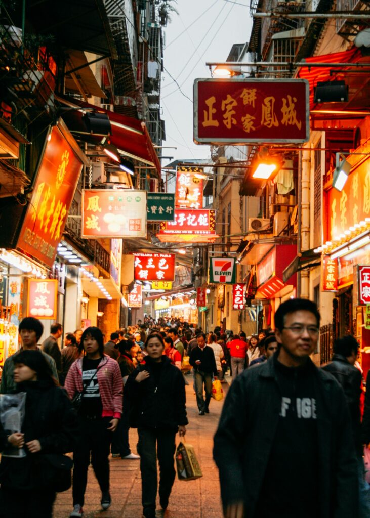 Vibrant street market in Macao with a crowd exploring shops and neon signs at night.