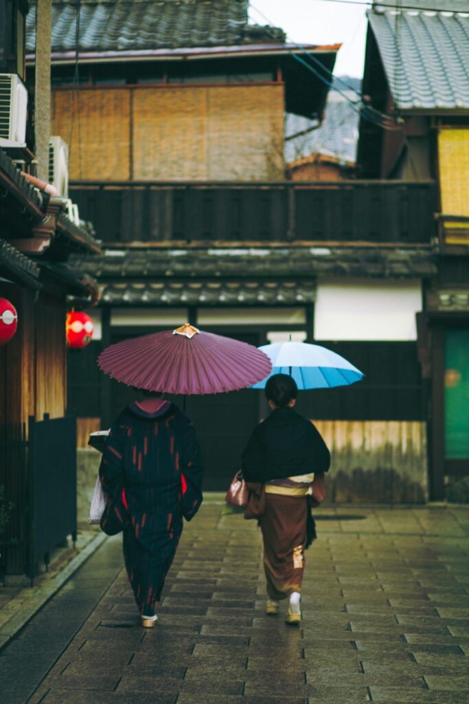 Couple in traditional attire strolling a Kyoto street with colorful umbrellas.