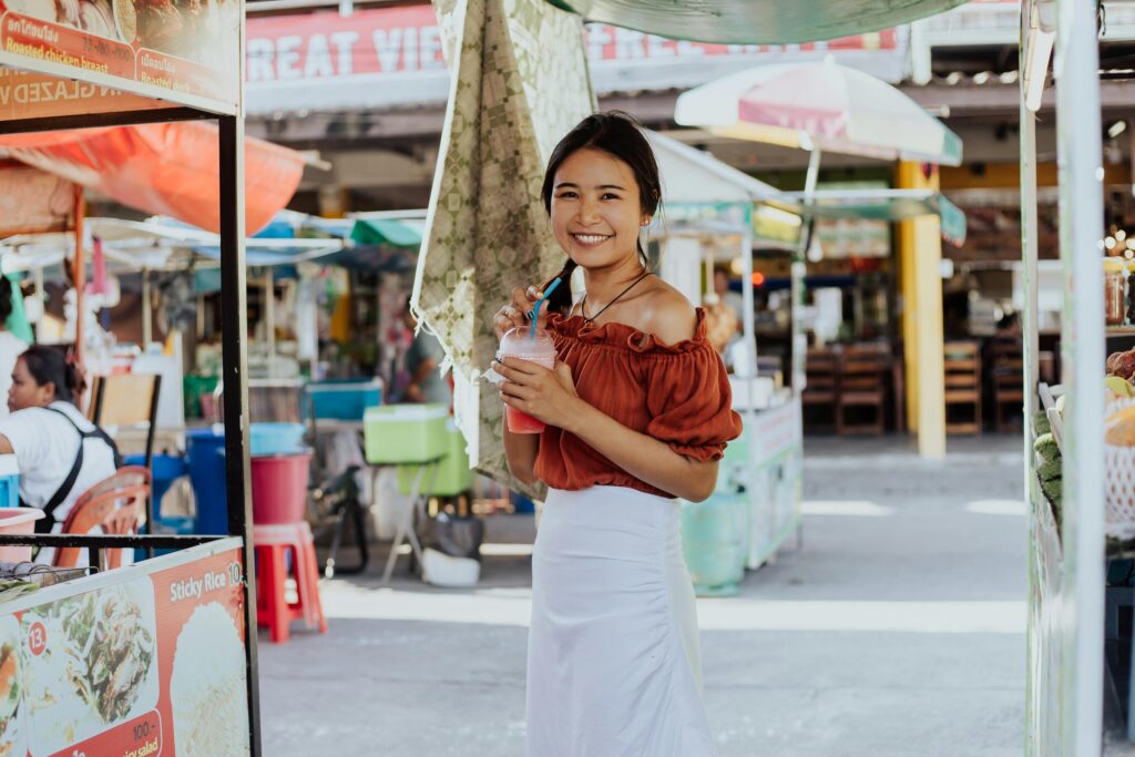 Cheerful woman holding a drink, enjoying her time at a vibrant Thai street market.