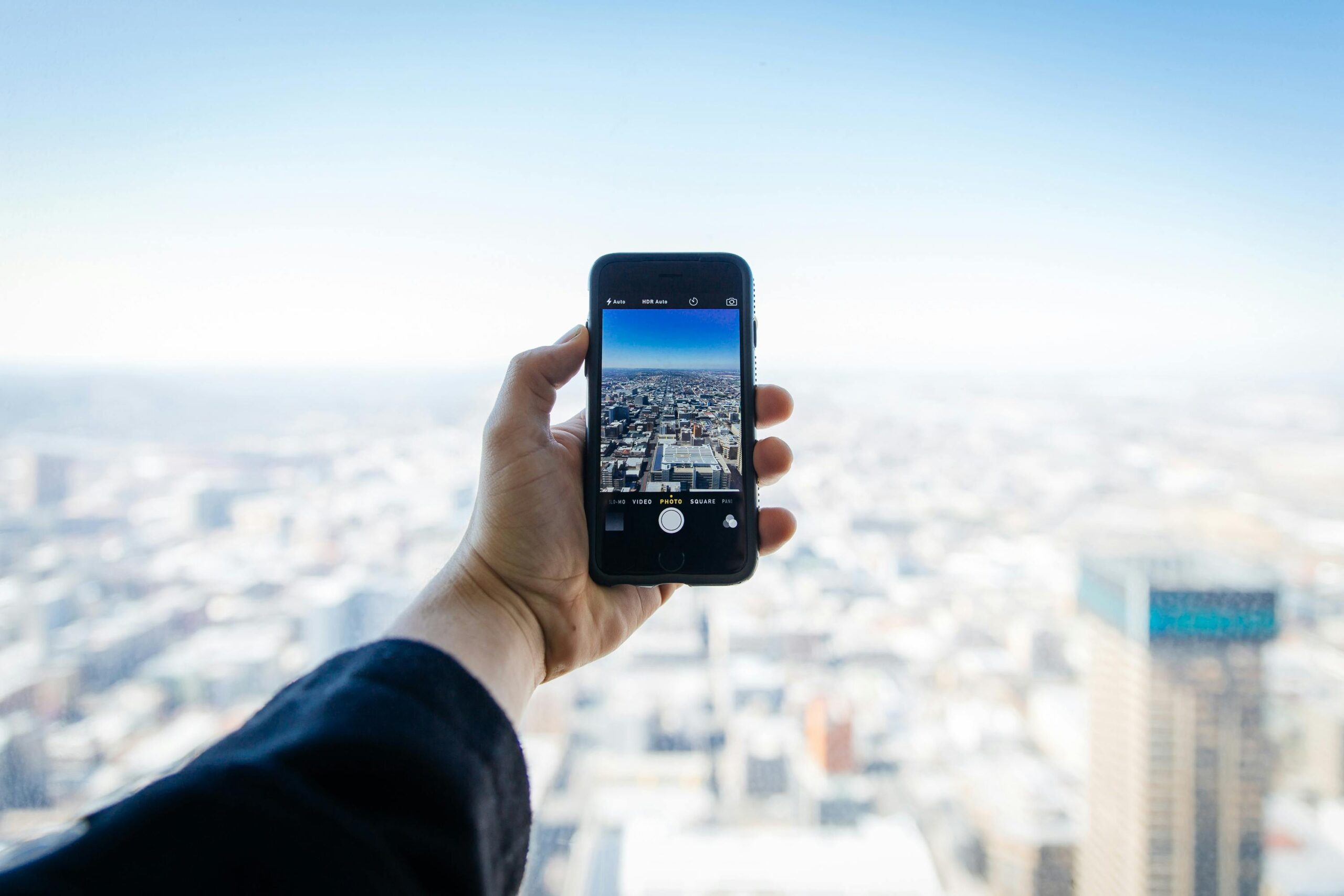 A hand holding a smartphone capturing an urban cityscape from above.